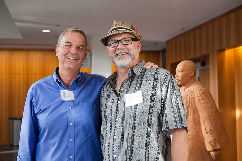Two people smile for the camera. They stand in front of the Martin Luther King Jr statue in the King Hall lobby.