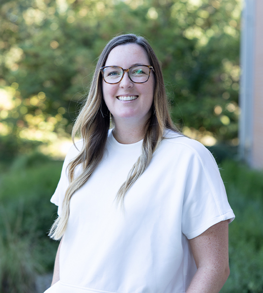 Ali Goff wearing a white blouse and eyeglasses. She is smiling at the camera.