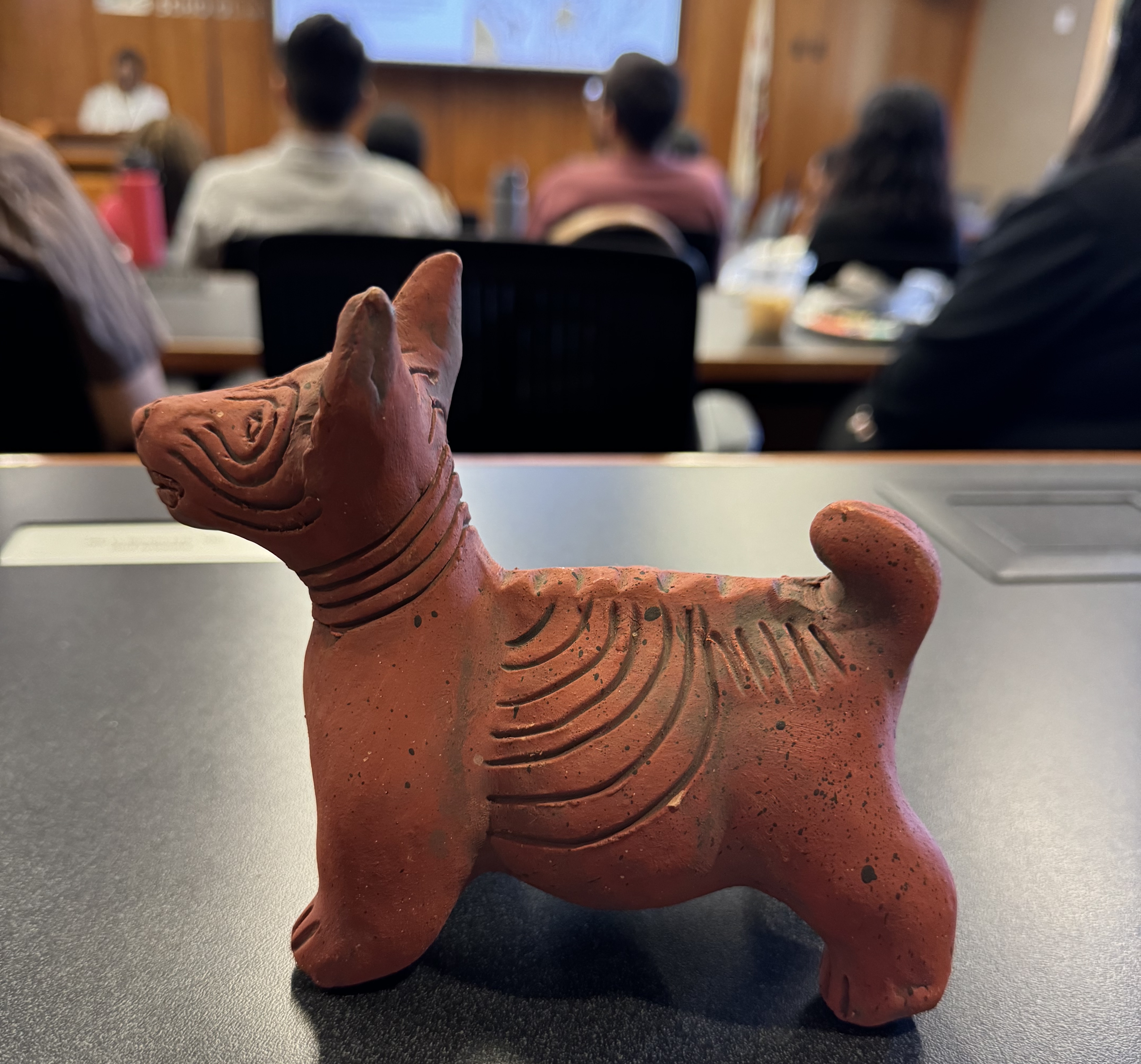 A reddish and brown ceramic statue of a dog on top of a table.