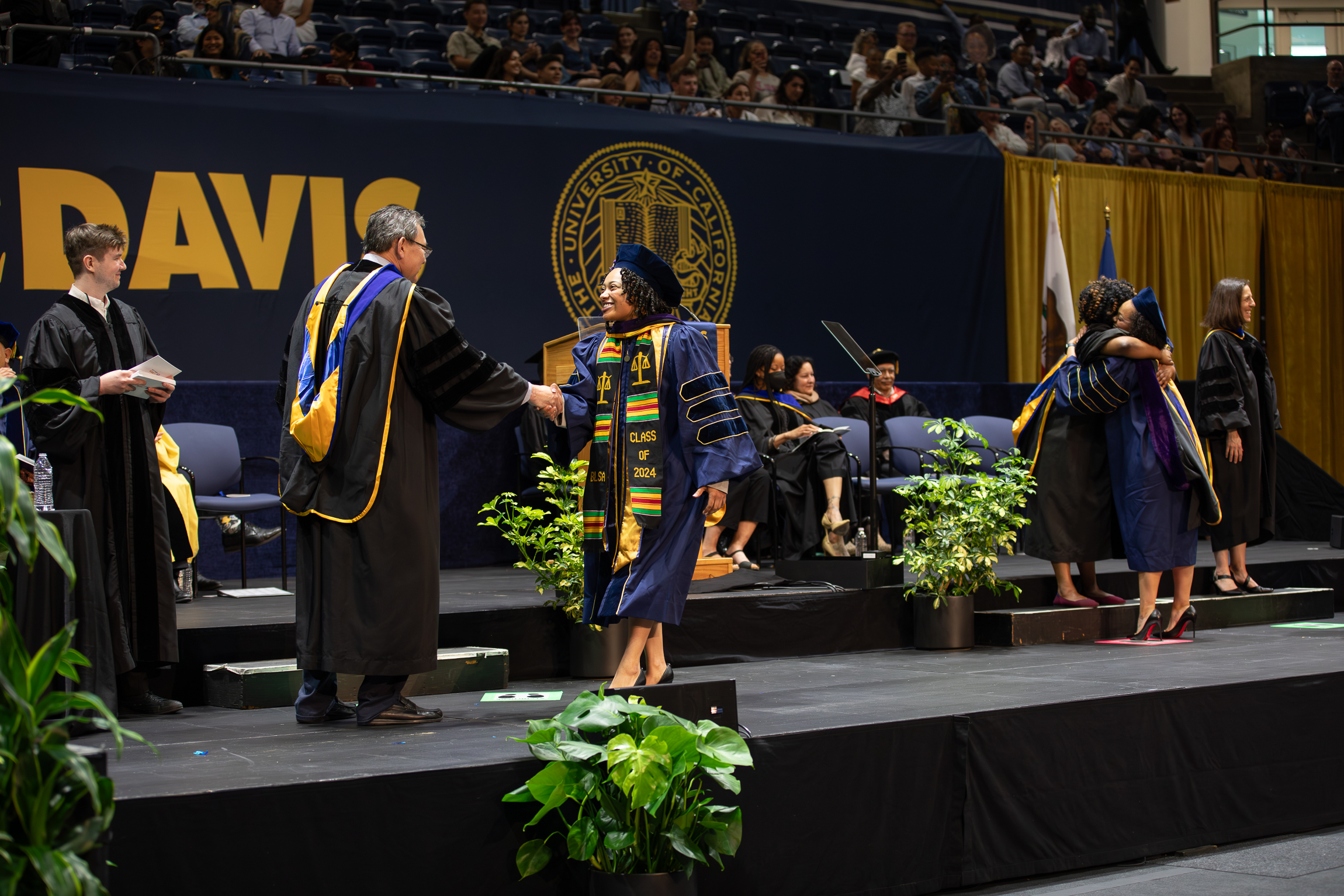 A graduate shaking Dean Kevin Johnson's hand on the stage at the UC Davis School of Law commencement ceremony.