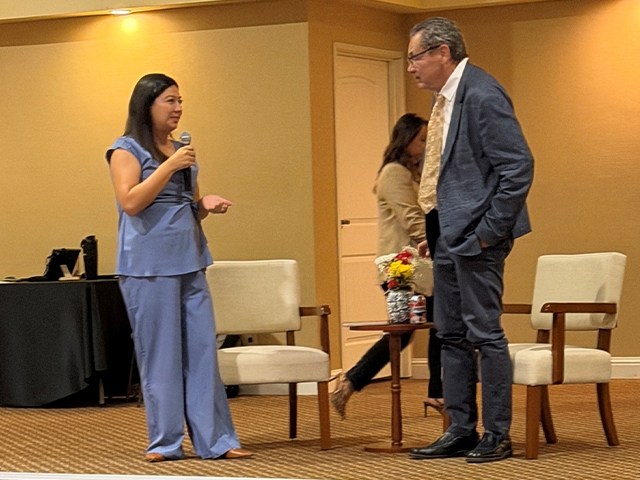 Woman in blue speaking into microphone to a man in a suit in a conference room.