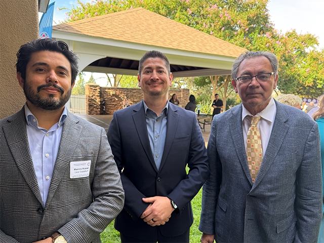 Three men in suits smiling at an outdoor event.