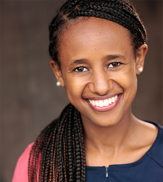 Roza Patterson wearing a blue blouse and pink cardigan. She is smiling brightly at the camera.