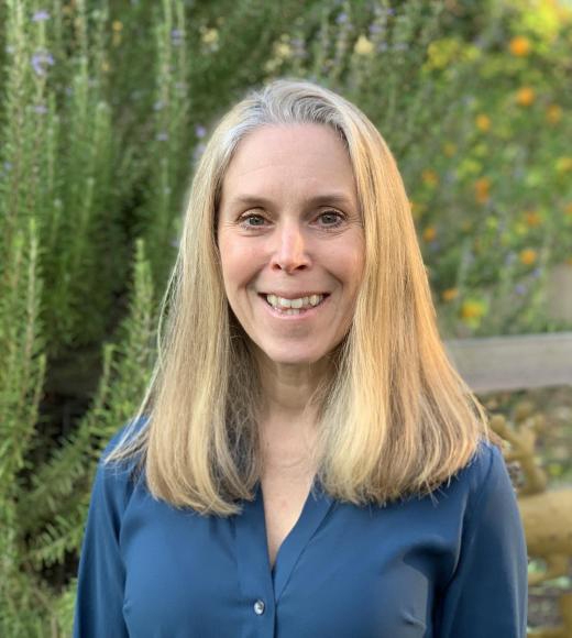 CELPC co-director Tracy Winsor wearing a blue blouse. She is smiling at the camera and there are green trees behind her.
