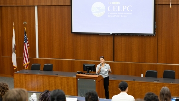 Speaker at podium in wood-paneled lecture hall, audience and projected CELPC logo