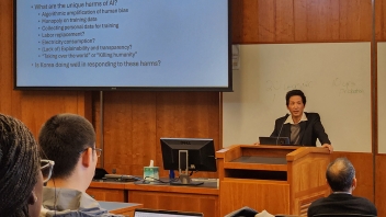 Lecturer speaking at podium in classroom with projected slide and seated audience
