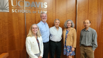 Five people smiling before a wood-paneled UC Davis School of Law sign