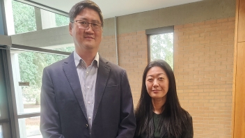 Professionally dressed man and woman standing by indoor window and brick wall