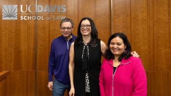 Three smiling adults standing before a wood-paneled wall with UC Davis School of Law logo