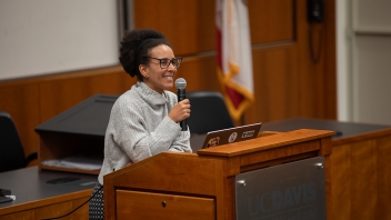 Smiling woman speaking into microphone at wooden podium in lecture hall