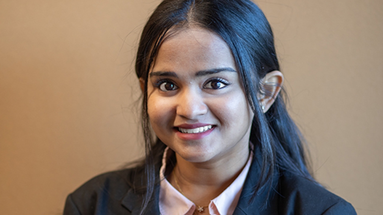A smiling woman in a black blazer and light shirt, posing against a plain background.