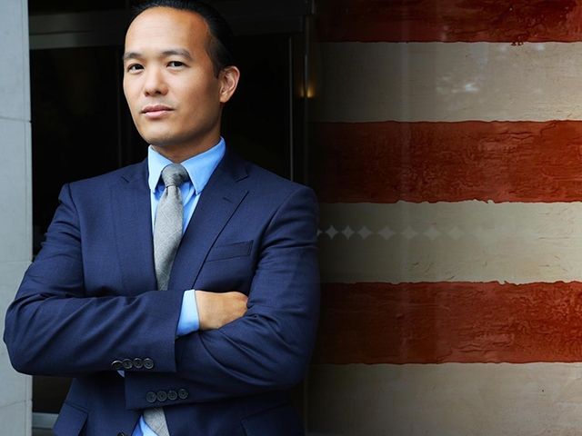 A graphic showing Professor Aaron Tang standing to the left-hand side of the American flag in the background. Professor Tang is wearing a suit and his arms are crossed.