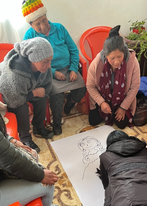 One woman draws on a sheet of paper on the floor while other women watch.