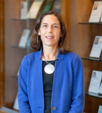 UC Davis Law Professor Courtney G. Joslin wearing a black blouse and blue cardigan. She is standing in front of a bookshelf.