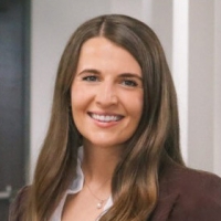 Smiling woman with long brown hair in a brown blazer, office headshot