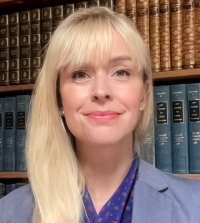 Acting Professor of Law Sarah Polcz wearing a blue blazer and standing in front of a bookshelf.