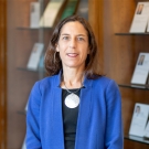 UC Davis Law Professor Courtney G. Joslin wearing a black blouse and blue cardigan. She is standing in front of a bookshelf.