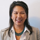 Jenny Huang smiling. She is wearing a gray blazer, white button down, and a turquoise necklace.