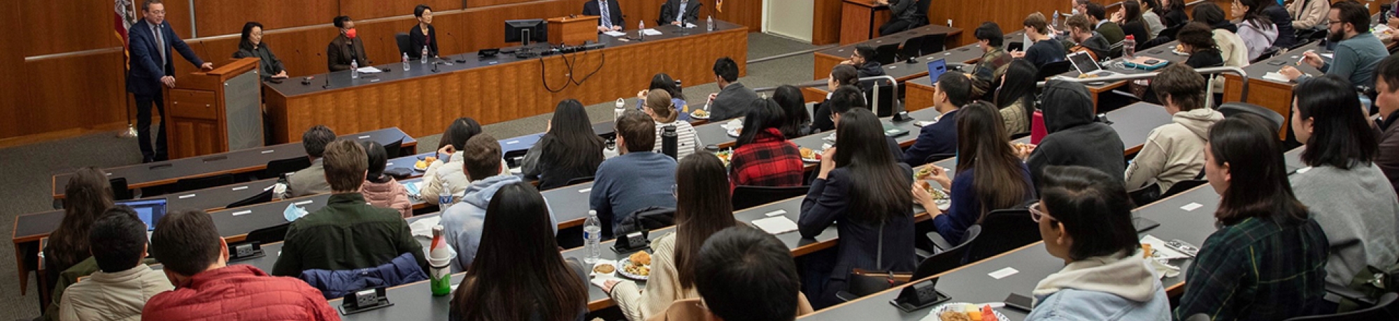 Lecture hall with students listening to speaker at podium; CILS logo on projection screen.